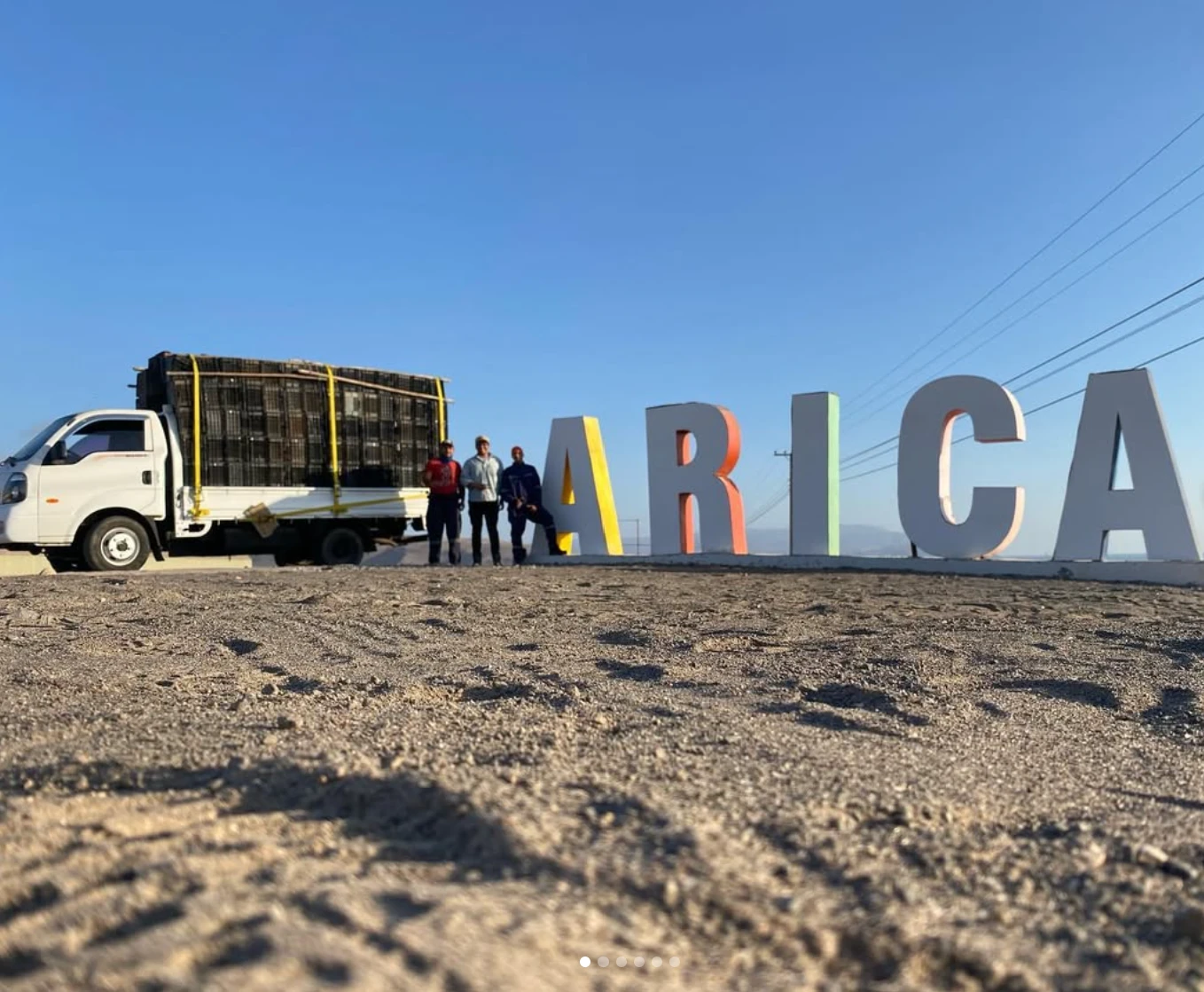 Camión cargado con cajas Onvert junto al letrero de Arica, con tres trabajadores