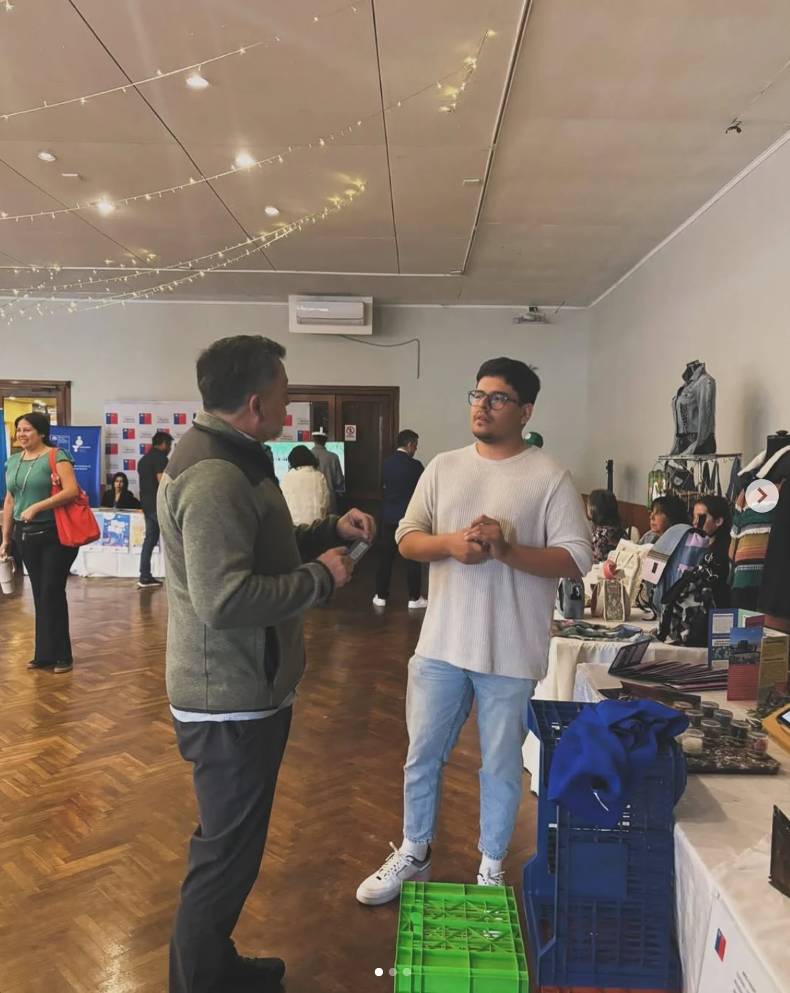 Conversación con un visitante en una feria de emprendimiento, junto a cajas Onvert verde y azul